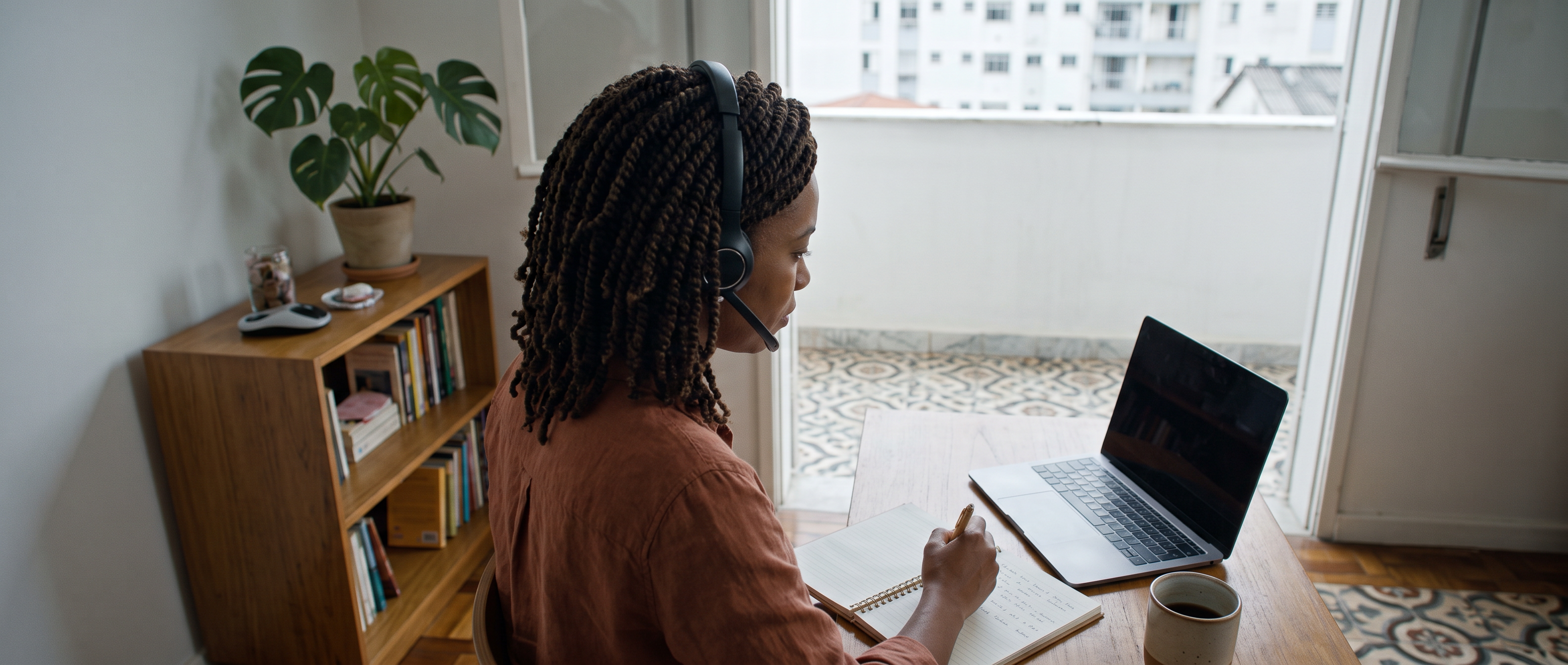 Recruiter listening through a headset and taking notes in a São Paulo home workspace.